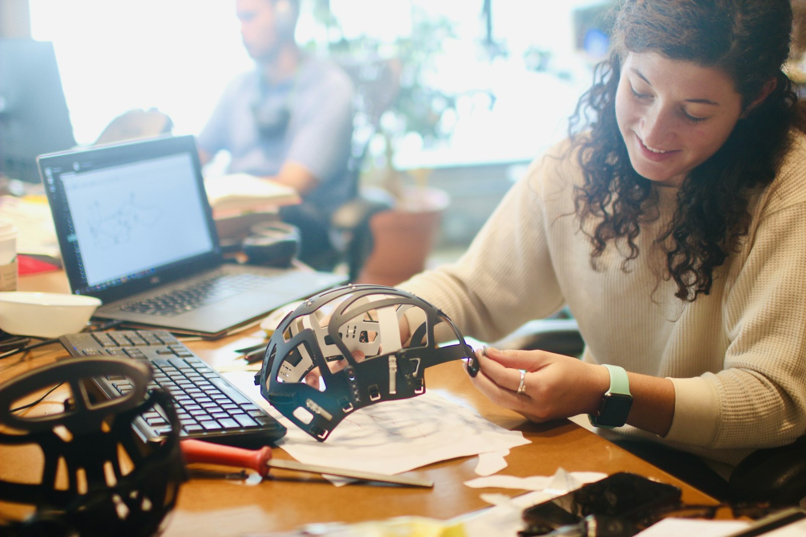 An engineer works on a helmet prototype at a desk